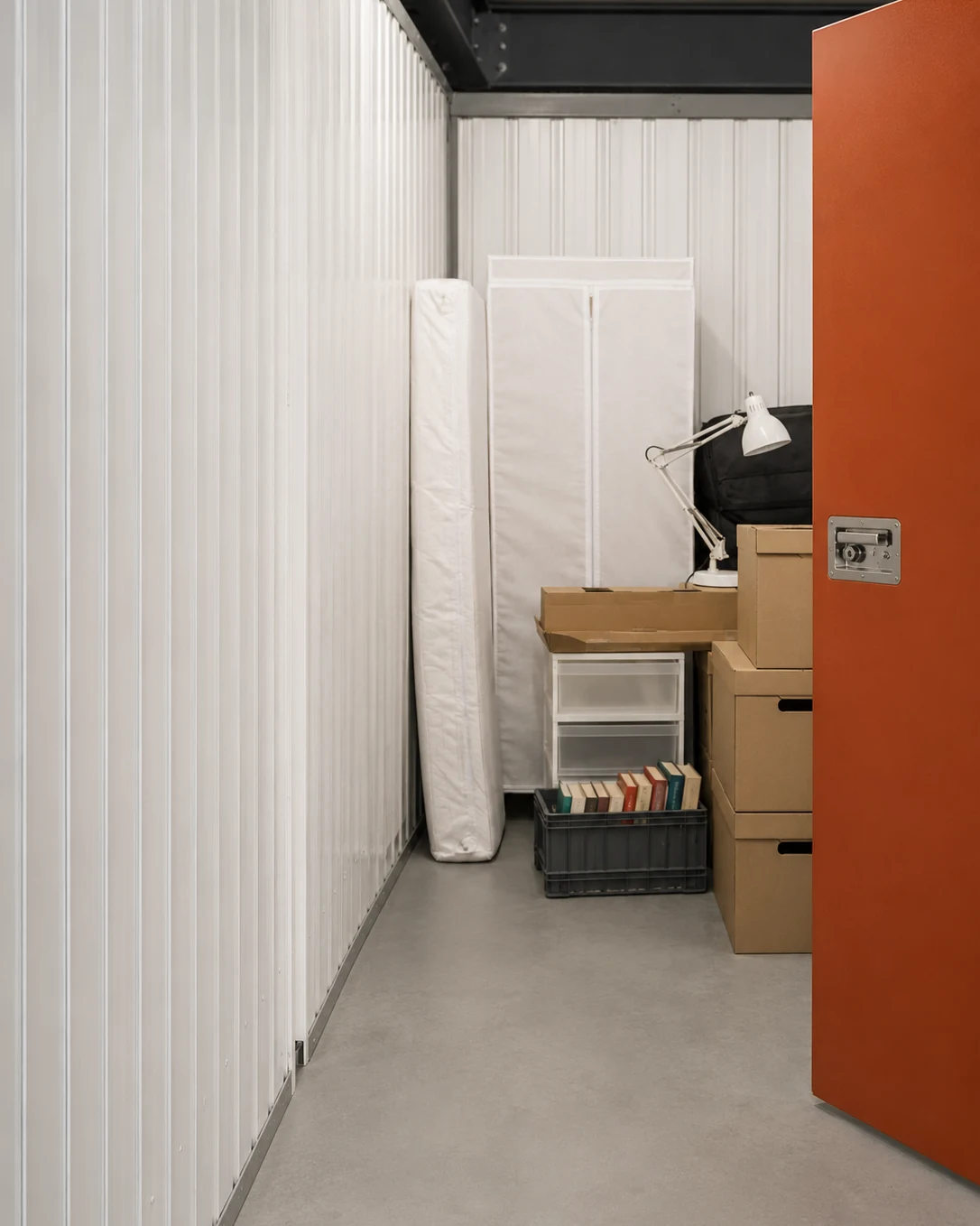 Studi-Hausstand in einer kleinen Lagerbox — Kisten, Bücherstapel und Schreibtischlampe